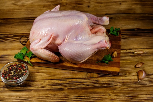 Frango inteiro cru com especiarias em uma mesa de madeira