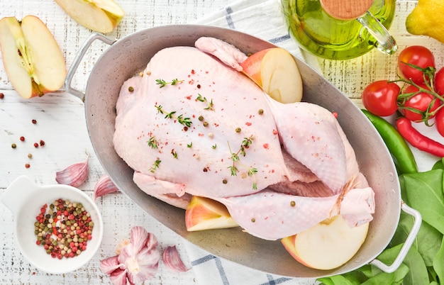 Frango inteiro cru com ingredientes para fazer pimenta rosa, limão, tomilho, alho, tomate cereja, azeda e sal na cozinha sobre fundo de ardósia cinza claro, pedra ou concreto. vista do topo. copie o espaço