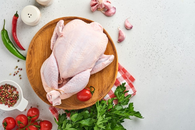 Frango inteiro cru com ingredientes para fazer pimenta rosa, limão, tomilho, azeda, tomate cereja e alho e sal na cozinha em pedra ardósia cinza clara ou fundo de concreto. Vista superior com espaço de cópia