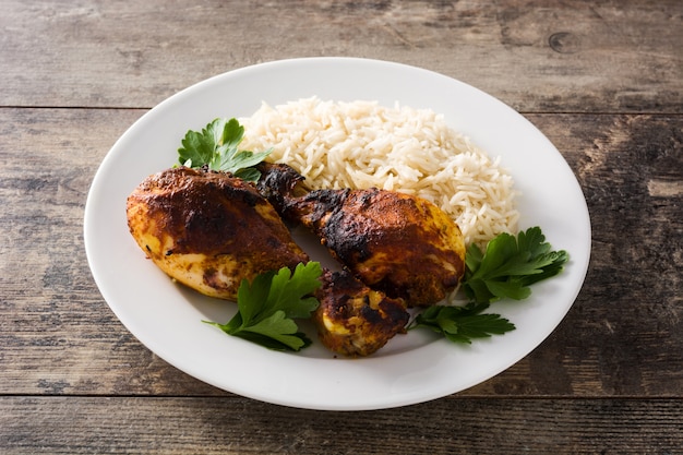 Frango tandoori assado com arroz basmati no prato na mesa de madeira.