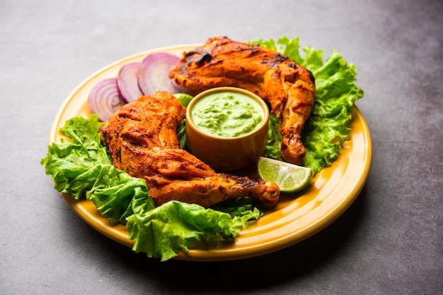 Frango Tandoori é um prato de frango preparado assando frango marinado em iogurte e temperos em tandoor ou forno de barro, servido com cebola e chutney verde