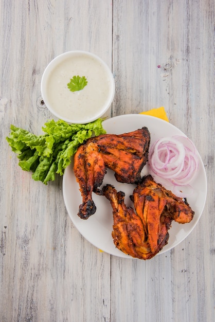 Frango tandoori - preparado assando frango marinado em iogurte e temperos em um tandoor. pedaço de perna servido em um prato com salada sobre fundo colorido ou de madeira. foco seletivo