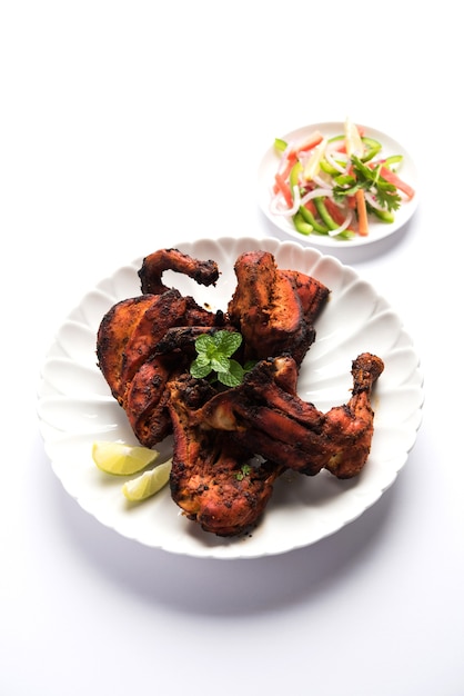 Frango Tandoori - preparado assando frango marinado em iogurte e temperos em um tandoor. Pedaços de perna servidos em prato com salada e chutney