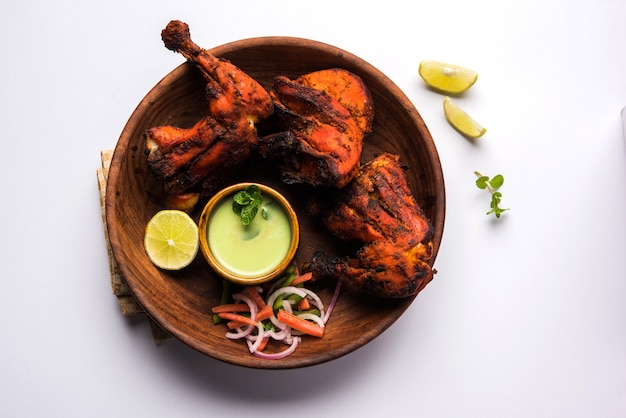 Frango Tandoori - preparado assando frango marinado em iogurte e temperos em um tandoor. Pedaços de perna servidos em prato com salada e chutney