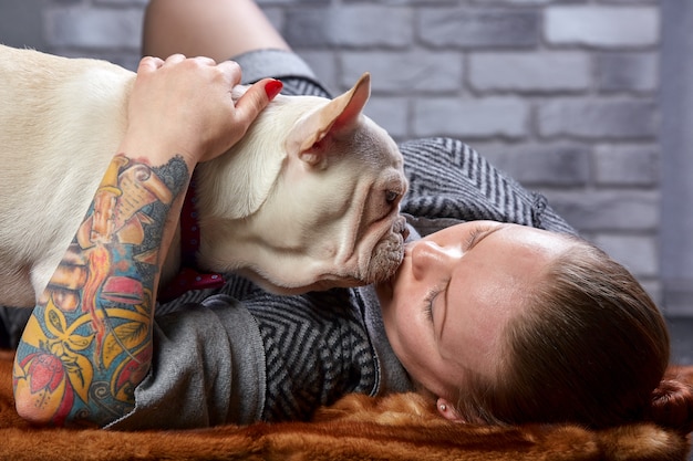 Französische Bulldogge auf den Händen seines Meisters. Es ist zu spüren, dass die Frau ihr Haustier liebt und es umarmt und fest küsst.