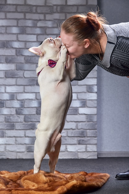 Französische Bulldogge auf den Händen seines Meisters. Es ist zu spüren, dass die Frau ihr Haustier liebt und es umarmt und fest küsst.