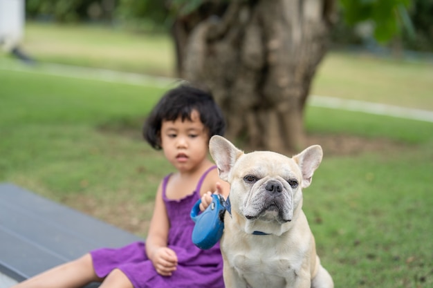 Französische Bulldogge sitzt auf einer Bank mit kleinem Mädchen in Violett gekleidet