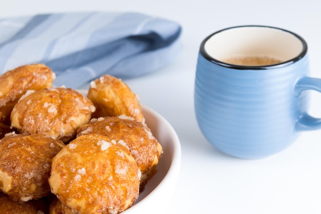 Französische Chouquettes puffs mit Zuckerperlen auf dem Teller mit blauer Tasse Kaffee Choux Gebäck klassisch