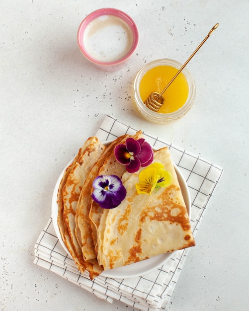 Französische Crepes, mit Blumen verzierte Pfannkuchen, eine Tasse Cappuccino und Honig. Konzept des Frühstücks, Dessert.