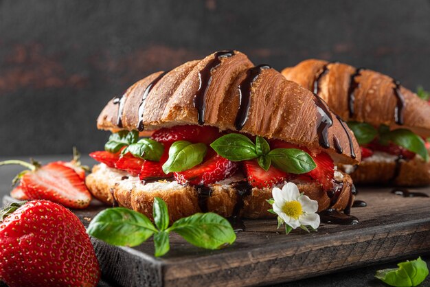 Französische Croissant-Sandwiches mit frischen Erdbeeren, Frischkäse, Basilikum und Schokoladensauce auf dunkler Oberfläche