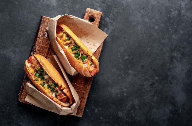 Französische Hot Dogs aus dem Laden in Papier verpackt, mit Käse und Senf auf Steinhintergrund gebacken
