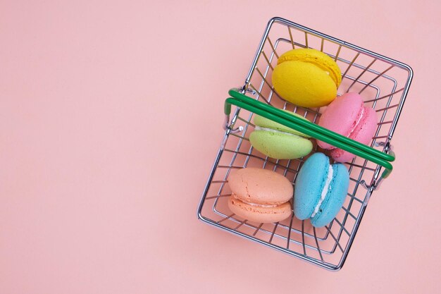 Französische Macarons-Kekse im Einkaufskorb auf rosa Hintergrund