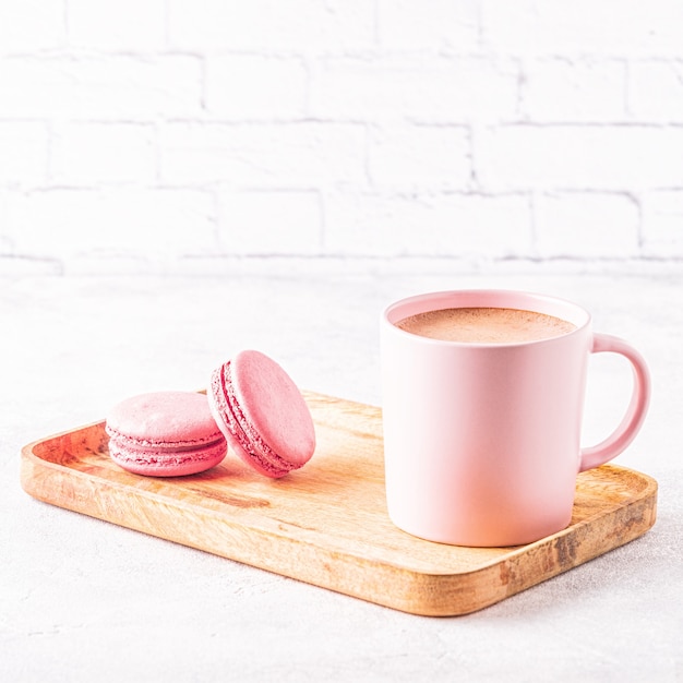 Französische Makronen und eine Tasse Kaffee auf einem Holztablett.