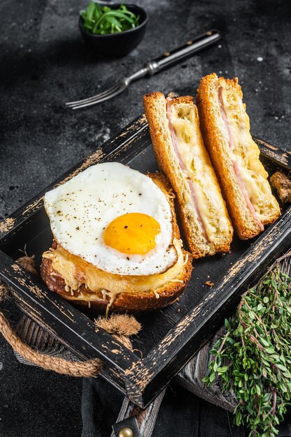 Französische Toasts Croque Monsieur und Croque Madame mit geschnittenem Schinken, geschmolzenem Emmentaler und Ei. Schwarzer Hintergrund. Ansicht von oben.