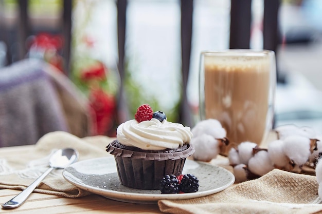 Französischer gluten- und zuckerfreier Himbeer- und Blaubeer-Cupcake und eine Tasse Latte Gemütliches Herbstfrühstück auf der Terrasse