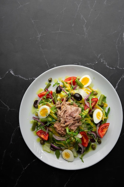 Französischer Salat Nicoise mit Thunfisch, Ei, grünen Bohnen, Tomaten, Oliven, Salat, Zwiebeln und Sardellen auf grauem Hintergrund Gesunde Ernährung