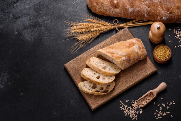 Französisches Baguettebrot, geschnitten auf einem Holzschneidebrett vor dunklem Betonhintergrund