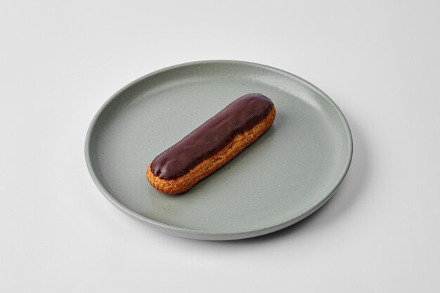 Französisches Eclair mit Schokoladenglasur auf einem Teller auf grauem Hintergrund