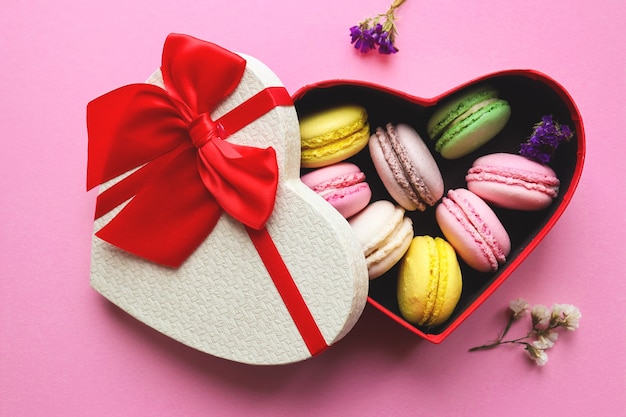 Französisches Makronengebäck in der herzförmigen Geschenkbox auf pastellrosa Hintergrund. Süßigkeiten für Valentinstag