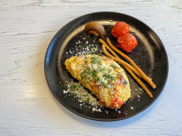 Französisches Omelett mit Speck, Tomaten, Pilzen und Käse auf einem schwarzen Teller