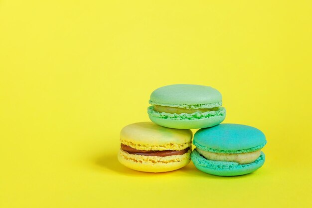 Französisches süßes Plätzchen-Minimal-Food-Bäckerei-Konzept rosa blau gelb grün macaron auf gelbem Hintergrund