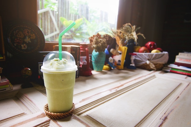 Foto el frappe de la leche del té verde en vidrio plástico transparente tiene paja verde en el estante de madera.