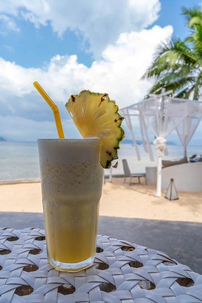 Frappe de piña fresca en la mesa con vista a la playa y cielo azul en verano