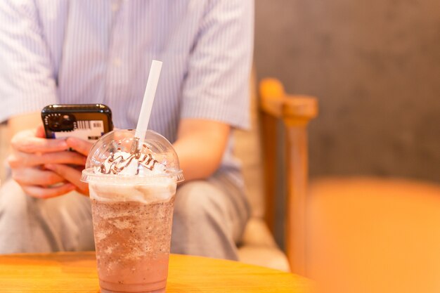 Frappuccino de café mezclado con paja de papel y personas que usan teléfono celular