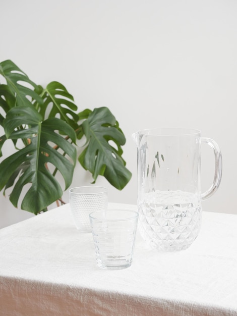 Frasco con agua dulce y vasos de cristal en la mesa con mantel planta verde en el fondo con espacio para copiar