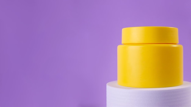 Frasco amarelo de creme em um pódio branco sobre um fundo roxo Aparência elegante do produto