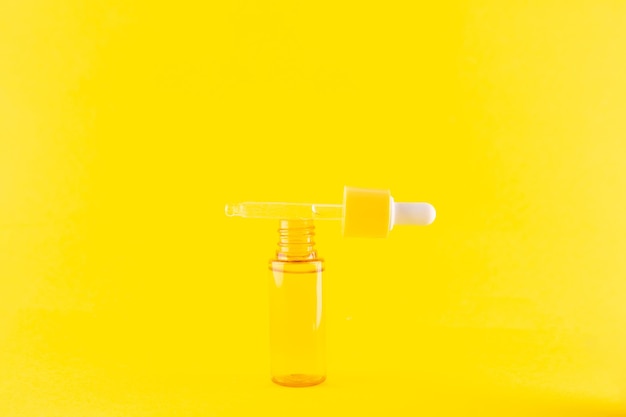 Frasco amarelo de vidro com pipeta com óleo essencial na vista superior de fundo amarelo Cosmético aromático