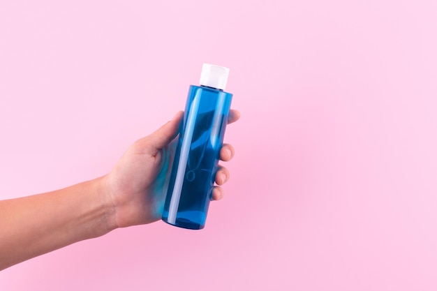 Frasco azul sem marca para água micelar de soro isolado fundo rosa Tubo de plástico na mão feminina