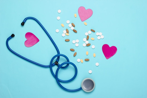 Frasco com diferentes pílulas, coração e estetoscópio em azul