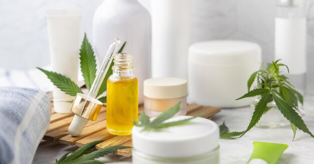 Frasco conta-gotas com óleo CBD e frascos de creme com folhas verdes de cannabis fechadas