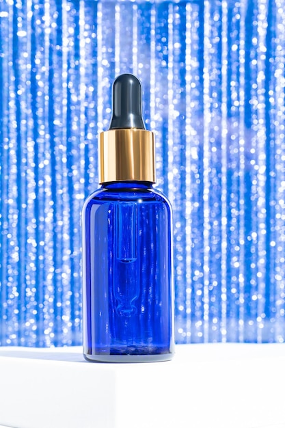 Frasco conta-gotas de pipeta com óleo facial de beleza em um fundo azul cintilante conceito de presente de tratamento de rosto e corpo