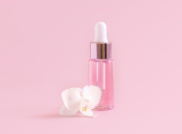 Frasco conta-gotas rosa perto da flor de orquídea branca em rosa claro perto do produto de beleza Skincare