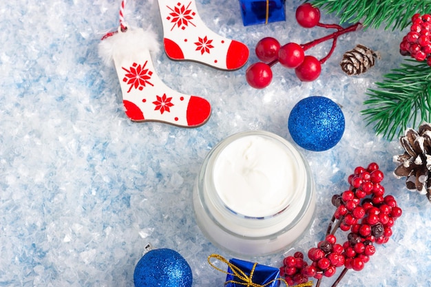 Frasco cosmético aberto com creme para o rosto e outros produtos de beleza em um fundo azul com decorações de natal produtos de cuidados com a pele de inverno banner de natal com espaço de cópia para texto