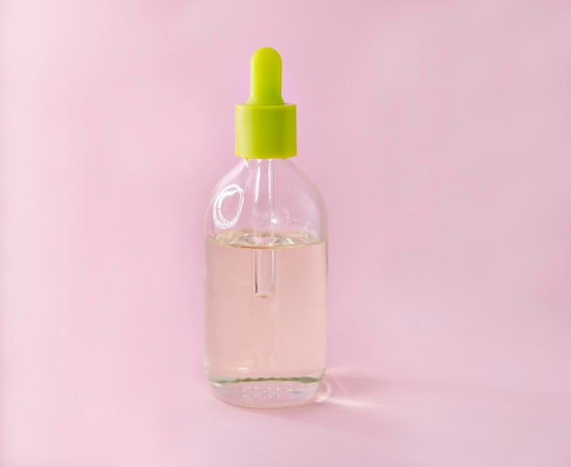frasco cosmético com sabonete líquido rosa e um copo de água, isolado no fundo branco.
