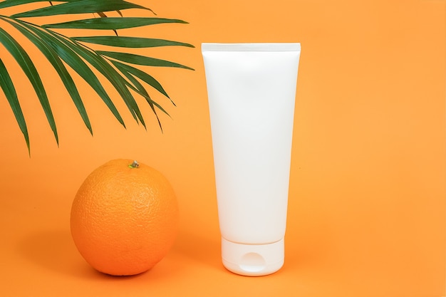 Frasco cosmético em branco branco, tubo de creme, loção para o corpo, rosto ou mão, fruta laranja e ramo de palma.