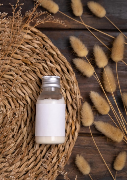 Frasco cosmético con etiqueta en blanco en el mantel de barbas boho cerca de la maqueta de hierba de cola de liebre