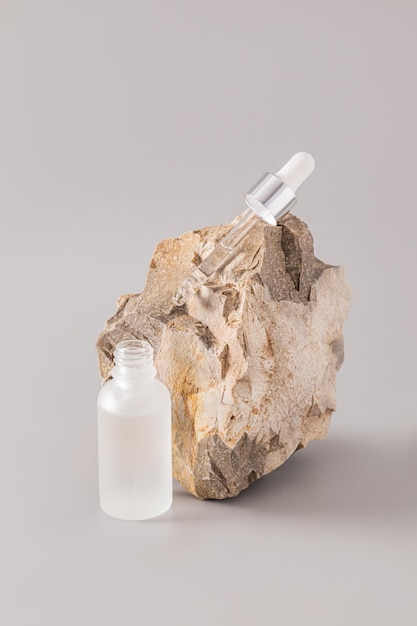 Un frasco cosmético mate transparente y una pipeta llena de un remedio natural se encuentran en una gran piedra texturizada Cosméticos de la naturaleza Cuidado natural