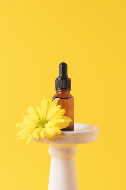 Frasco cosmético con pipeta cuentagotas y suero o aceite esencial en podio con flor amarilla Concepto de belleza para el cuidado facial y corporal