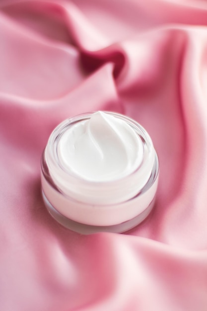 Frasco de crema facial de lujo en una seda rosa suave