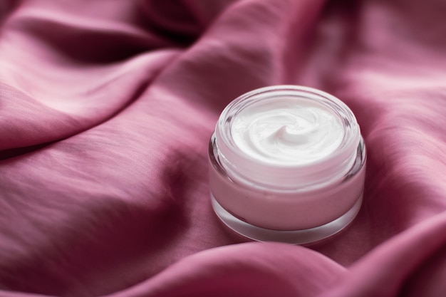 Frasco de crema facial de lujo en una seda rosa suave