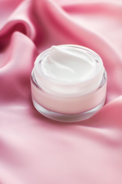 Frasco de crema facial de lujo en una seda rosa suave