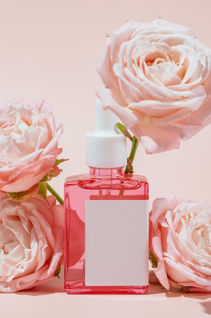 Foto frasco de cosméticos de vidro rosa com um gotinho em um fundo rosa entre flores de rosas em flor conceito de cosméticos naturais óleos essenciais naturais e produtos de cuidados com a pele