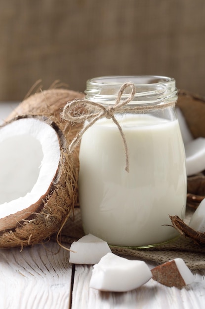 Frasco de leite ou iogurte em guardanapo de cânhamo na mesa de madeira branca com coco de lado