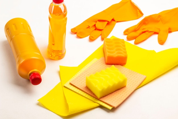 Frasco de líquido laranja, esponja amarela e pano amarelo. Produtos químicos domésticos para limpar o apartamento. Fundo branco. Vista do topo