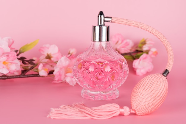 Frasco de perfume de vidro transparente com galho de árvore florescendo primavera em fundo rosa. frasco de essência aromática