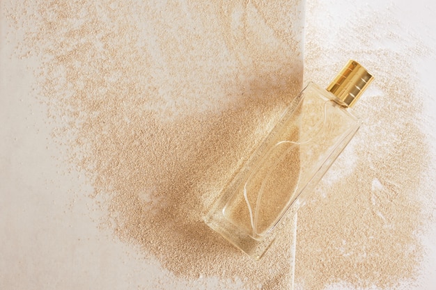 Frasco de perfume de vidro transparente com tampa dourada sem rótulo na areia fundo cópia espaço vista superior simulação de conceito cosmético